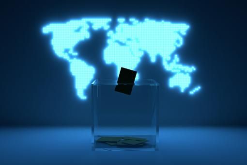 A transparent ballot box in front of a illuminated map of the world.